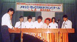 白いシャツを着た8人の男性が気でできた楽器を演奏している写真